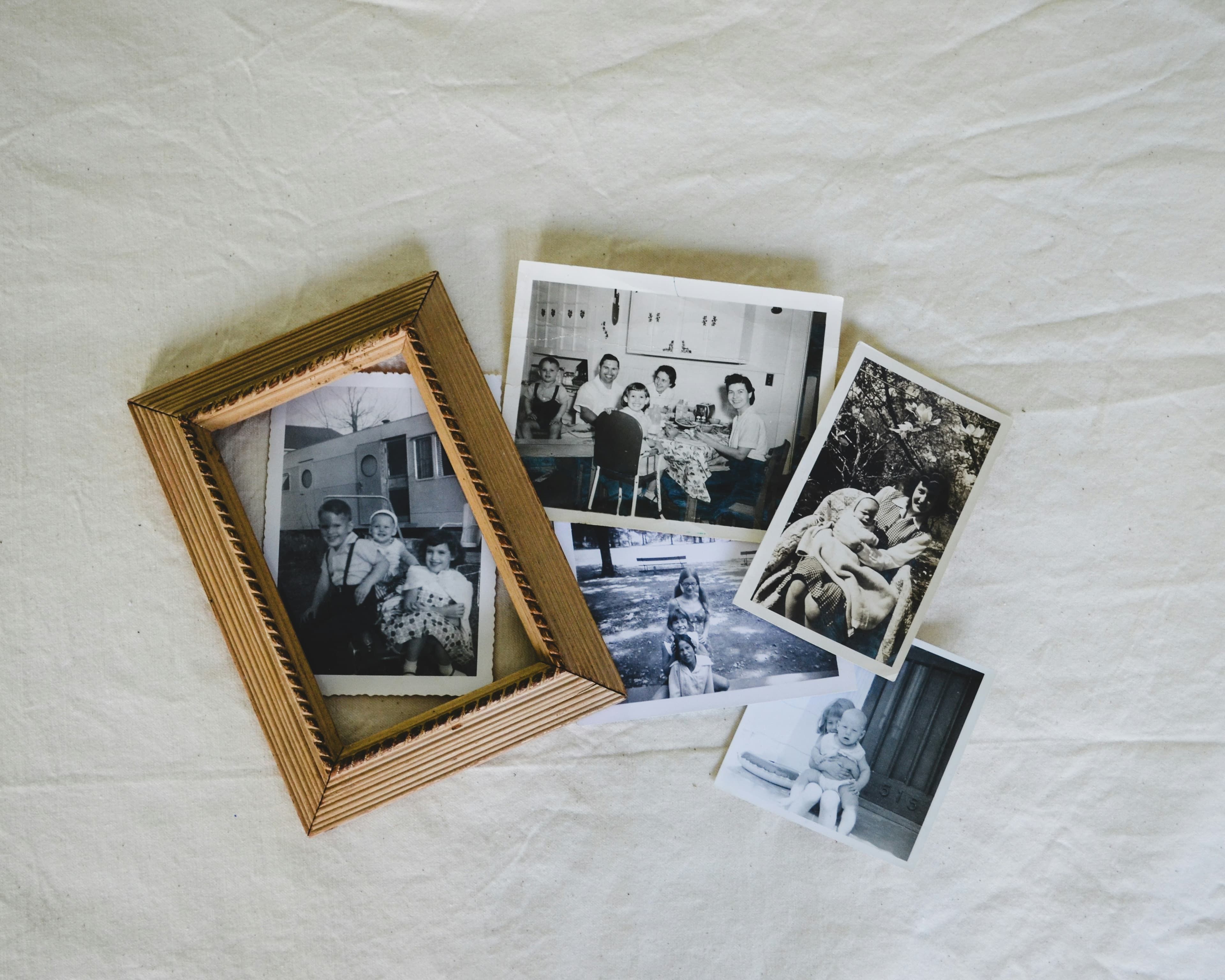 Photographies de famille en noir et blanc éparpillées, dont un portrait encadré, sur un tissu clair.